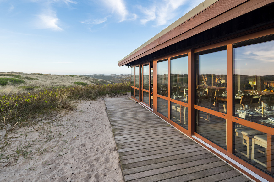 Besondere Herausforderungen der Sanierungsmaßnahmen der „Sansibar“ auf Sylt waren bauordnungsrechtliche Vorschriften zum Küsten- und Dünenschutz sowie ein ausreichender Schutz gegen Wind und Wetter.Im Bild: Hebe-Schiebesystem Schüco ASE 80.HI.