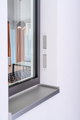 Das Zwei-Wege-Lüftungsgerät „Caire smart“ wird ins Fenstersystem integriert (seitlich oder oben, mit sichtbarem, farblich angepasstem Gehäuseprofil) und kann überdämmt und überputzt werden. - © Gealan
