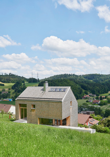 Die erdanliegenden Bereiche sind aus Sichtbeton mit einer Kiefersperrholzschalung strukturiert. Darüber sitzt – sich im Innenraum präzise ­verzahnend – ein Holzriegelbau, außen mit Schindeln und innen mit unbehandelter ­Täfelung und sägerauen Dielen aus Weißtanne verkleidet. - © Foto: Velux/Jürg Zimmermann